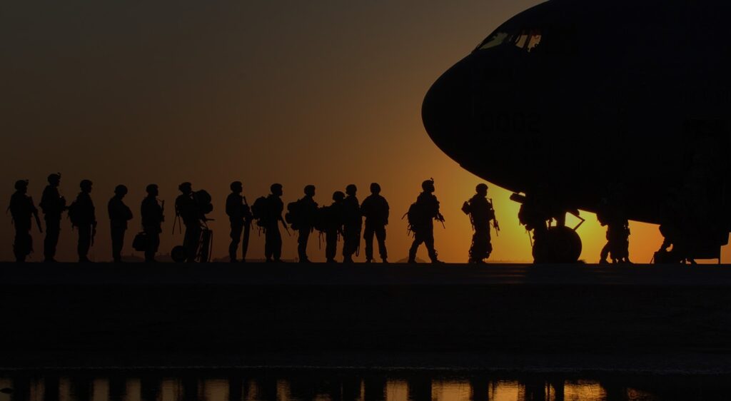 Service members silhouetted against a sunset as they board a military aircraft